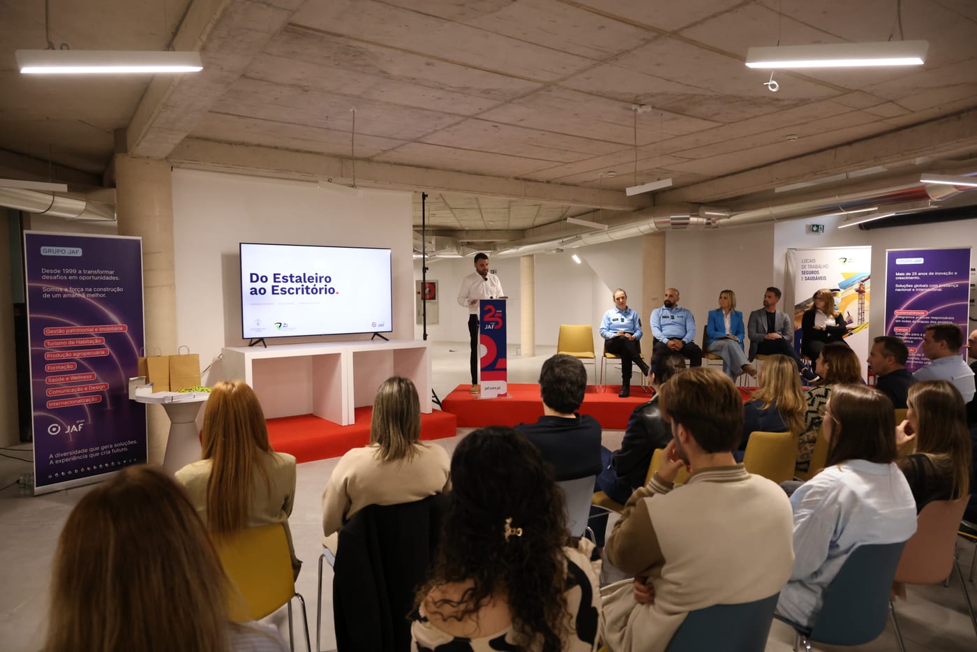 Audience of employees watching the presentation, with the screen showing the motto “From the Site to the Office”